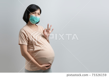 Smiling Asian Pregnant woman wearing protective face mask showing gesture OK sign Smiling Asian Pregnant woman wearing protective face mask showing gesture OK sign 73326159