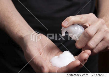 Closeup of a male hand with foam on the palm. man squeezes shaving foam onto his hand. Putting whip foam soap bottle with foam on man hand 73326568