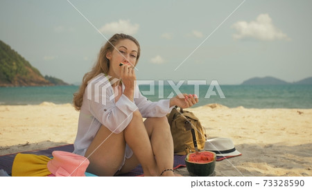 The cheerful woman in holding and eating slices of watermelon on tropical sand beach sea. Portrait attractive girl spend summer weekend. 73328590
