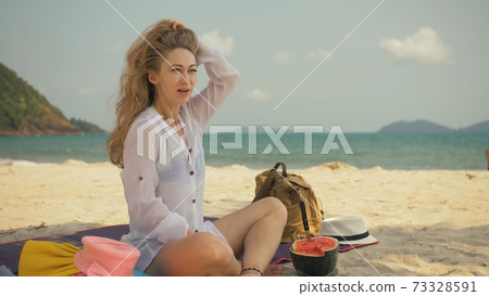 The cheerful woman in holding and eating slices of watermelon on tropical sand beach sea. Portrait attractive girl spend summer weekend. 73328591