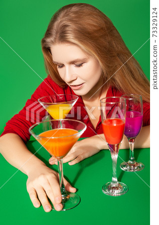 Young female with colorful alcohol drinks on green background 73329124
