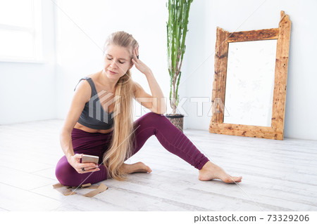 Sportswoman suing smartphone at home resting on floor Sportswoman suing smartphone at home resting on floor 73329206