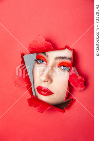 Woman with red visage looking through torn paper Woman with red visage looking through torn paper 73329343