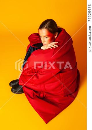 Lonely woman wrapping in baggy coat against yellow background Lonely woman wrapping in baggy coat against yellow background 73329488