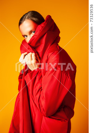 Young woman wrapping in red coat against yellow background Young woman wrapping in red coat against yellow background 73329536