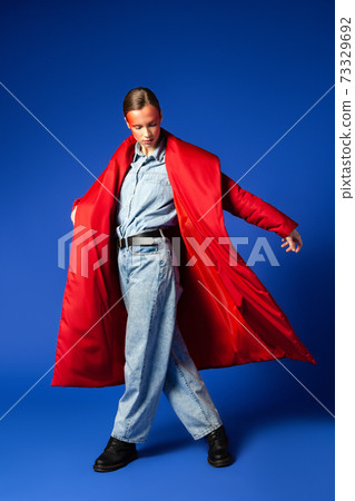 Woman in stylish coat dancing against blue background 73329692