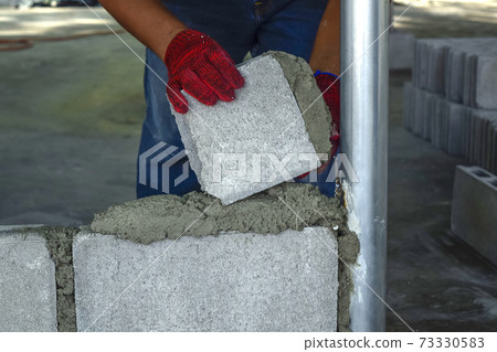 Plaster worker wearing red gloves is laying bricks. 73330583