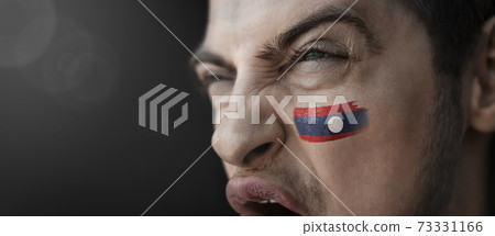 A screaming man with the image of the Laos national flag on his face 73331166