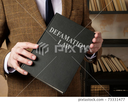 Lawyer in suit holds Defamation law book. 73331477