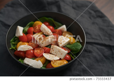 Salad with cherry tomatoes, spinach and mozzarella in black bowl on linen cloth Salad with cherry tomatoes, spinach and mozzarella in black bowl on linen cloth 73333437