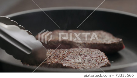 man flipping beef steak on nonstick pan with tongs 73333560
