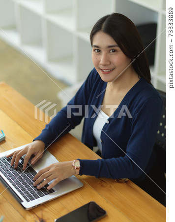 Portrait of female university student smiling to camera while doing assignment 73333889