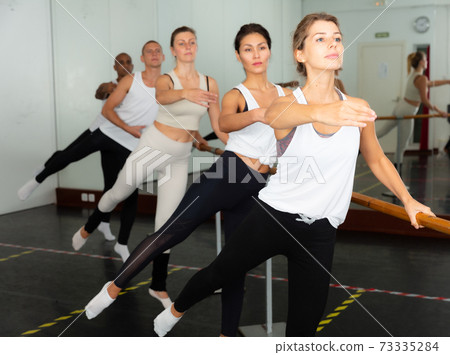 multiethnic dancers standing with one hand on barre 73335284