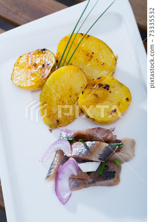 Fried potatoes with slices of mild-cured herring and onions served on plate Fried potatoes with slices of mild-cured herring and onions served on plate 73335532