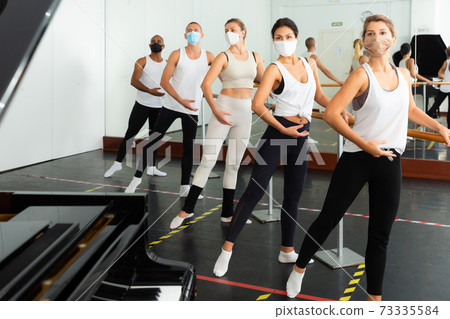 Dancers in medical masks training near barre during COVID-19 pandemic. Dancers in medical masks training near barre during COVID-19 pandemic. 73335584