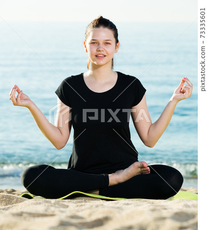 Female in black T-shirt is sitting and practicing meditation Female in black T-shirt is sitting and practicing meditation 73335601