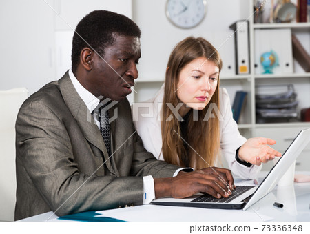 Male and female colleagues working with laptop and documents at table Male and female colleagues working with laptop and documents at table 73336348