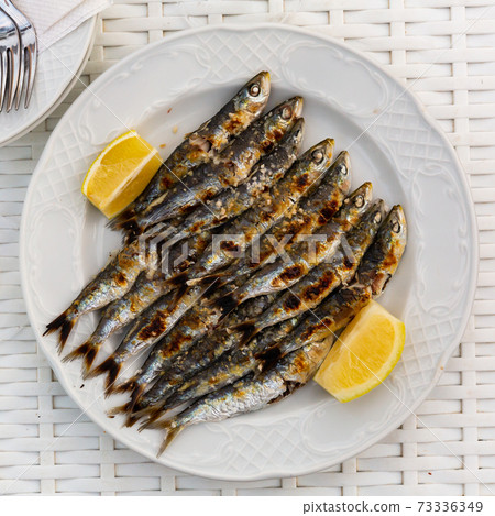 Malaga cuisine grilled sardines served with lemon on white plate on wooden table Malaga cuisine grilled sardines served with lemon on white plate on wooden table 73336349