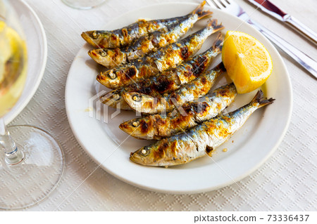 Malaga cuisine grilled sardines served with lemon on white plate on wooden table Malaga cuisine grilled sardines served with lemon on white plate on wooden table 73336437