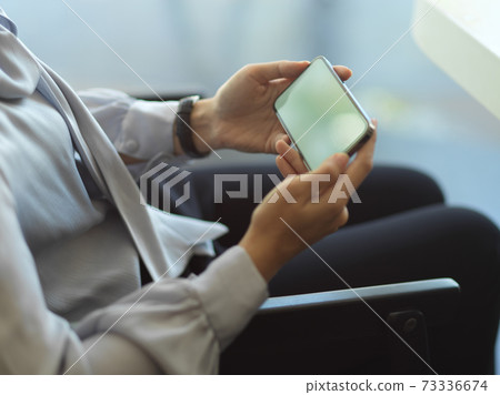 Female hand holding horizontal smartphone while relaxing in office room 73336674