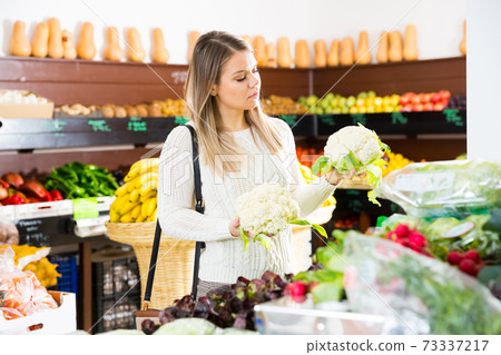 Woman choosing vegetables in greengrocery Woman choosing vegetables in greengrocery 73337217