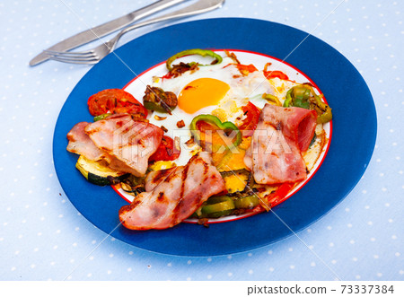 Scrambled eggs with bacon and vegetables served on plate Scrambled eggs with bacon and vegetables served on plate 73337384