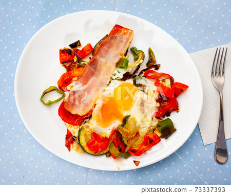 Scrambled eggs with bacon and vegetables served on plate 73337393