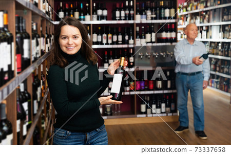 female customer selecting bottle of wine in shop 73337658