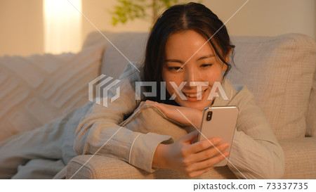 晚上看著她在沙發上的智能手機的年輕女子 晚上看著她在沙發上的智能手機的年輕女子 73337735