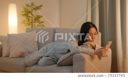 Young woman looking at a smartphone on the sofa at night Young woman looking at a smartphone on the sofa at night 73337743