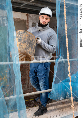 Guy carrying bucket of mortar at building site 73338015