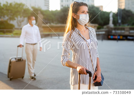 Young woman in medical mask walking around city with suitcase Young woman in medical mask walking around city with suitcase 73338049
