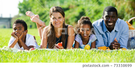 Couple with children lying on green lawn Couple with children lying on green lawn 73338699
