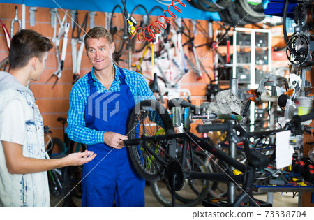 Adult seller repairing bike wheel and chatting Adult seller repairing bike wheel and chatting 73338704