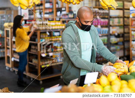 Hispanic man in protective mask looking for bananas in supermarket Hispanic man in protective mask looking for bananas in supermarket 73338707