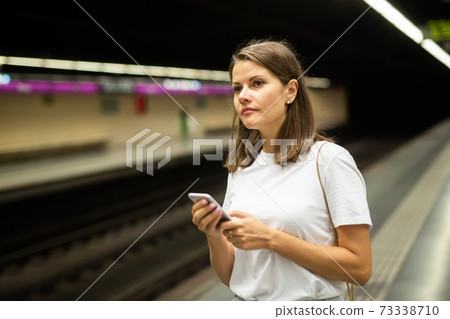 Woman waiting subway car using phone 73338710