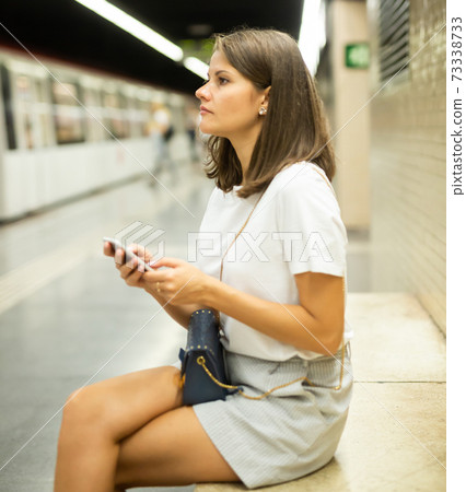 Woman waiting subway car using phone 73338733