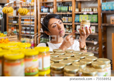Positive woman reads description of canned food at a supermarket 73338952