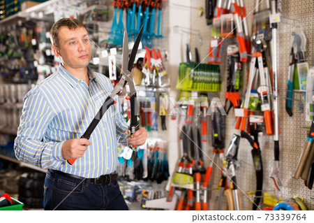 Happy male customer examining secateurs in garden equipment shop 73339764
