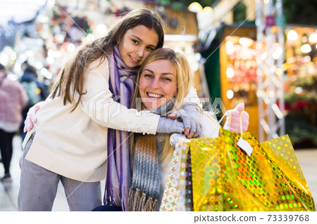 Happy mom and daughter with packages of gifts on street market Happy mom and daughter with packages of gifts on street market 73339768