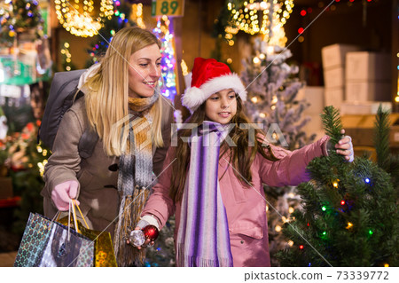 Family of mother and teen daughter having fun on outdoor fair, choosing fir tree for New Year celebration Family of mother and teen daughter having fun on outdoor fair, choosing fir tree for New Year celebration 73339772