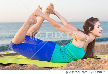 Smiling young woman in blue T-shirt is practicing stretching Smiling young woman in blue T-shirt is practicing stretching 73339894