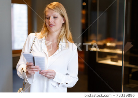 Female visitor with guide book looking at exhibition in museum Female visitor with guide book looking at exhibition in museum 73339896