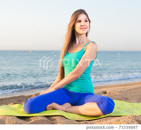 Female 20-25 years old is sitting and practicing meditation in blue T-shirt Female 20-25 years old is sitting and practicing meditation in blue T-shirt 73339897