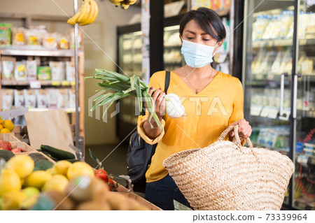 Woman in protective mask choosing greens in supermarket Woman in protective mask choosing greens in supermarket 73339964