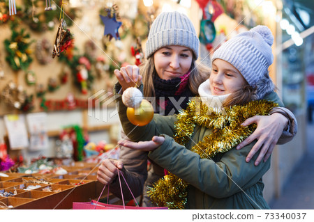 Young girl and her mother are choosing decorations for Christmas tree 73340037