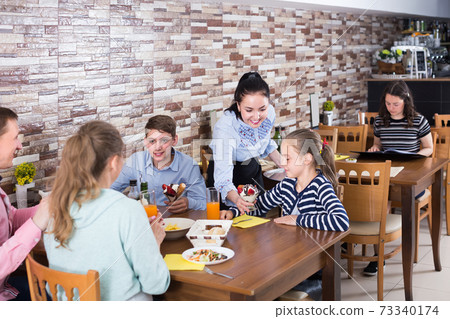 Polite cheerful waitress serving dishes to family Polite cheerful waitress serving dishes to family 73340174