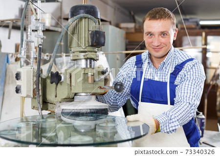 Craftsman working on machine for curved glass faceting 73340326