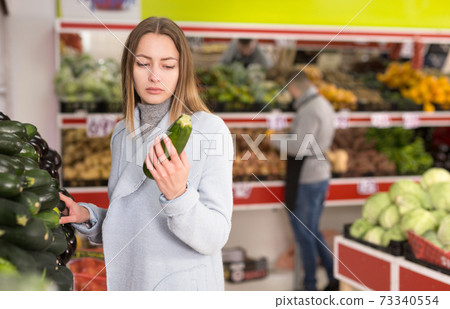 Female shopper picks cucumbers at grocery store Female shopper picks cucumbers at grocery store 73340554
