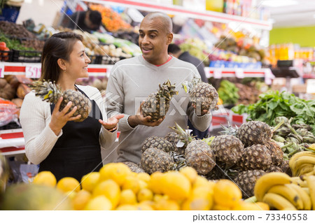 Female grocery salesperson advises man to buy pineapple 73340558